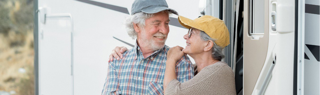 cheerful senior couple standing outside a caravan