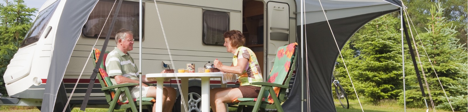 Two friends sitting outside the caravan under tent enjoying breakfast & nice weather.