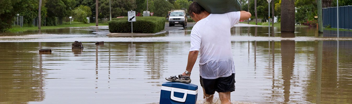 A man carrying his belonging through flood on the road.