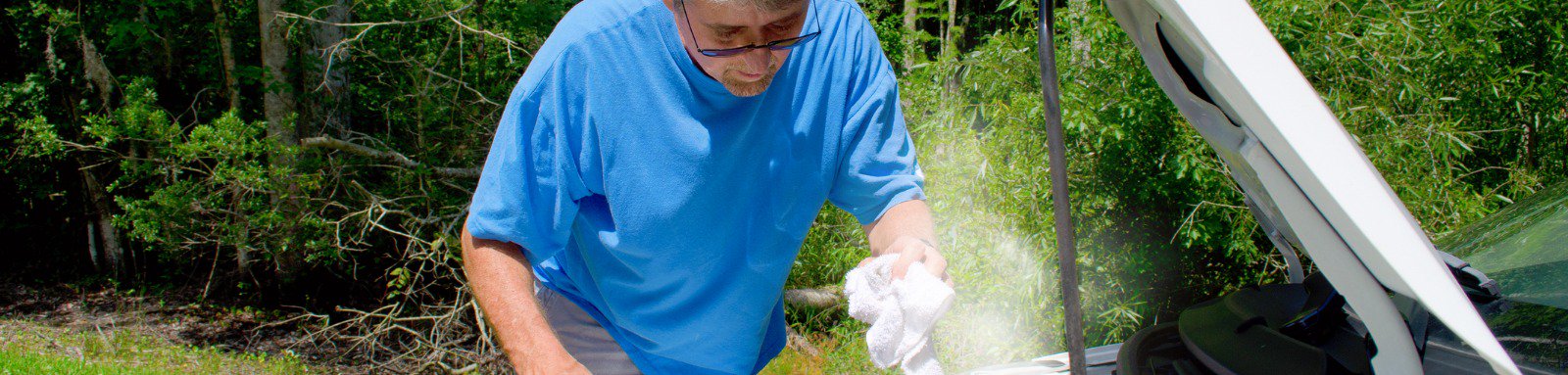 A man wearing blue t-shirt  & gloves fixing steam engine of car.