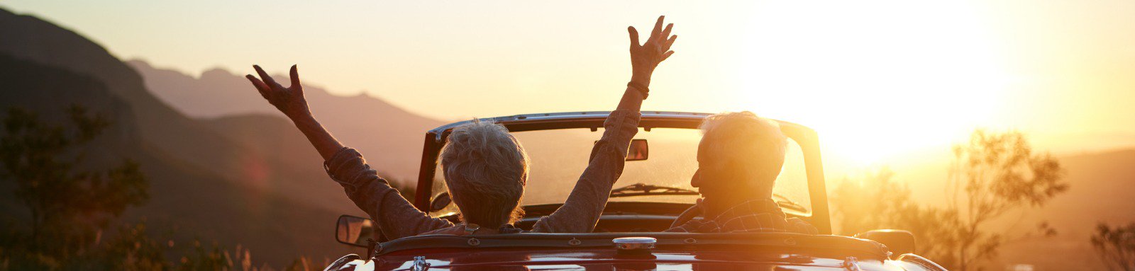 A mature couple is out on drive during sunset in convertible car.