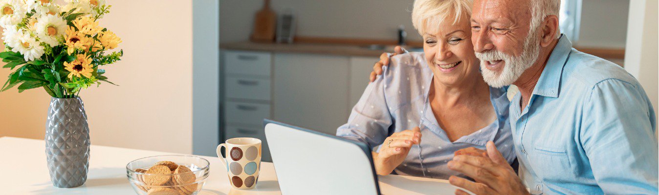 A retired couple sitting on chair & watching something on Laptop.