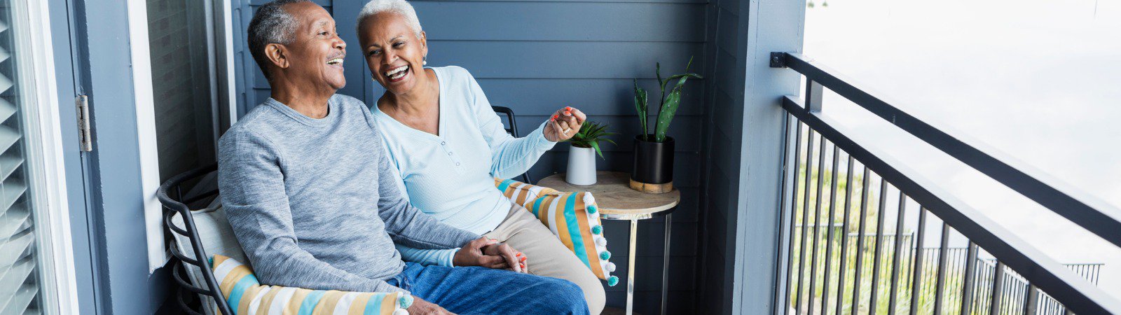 senior-couple-sitting-on-porch-holding-hands-laughing