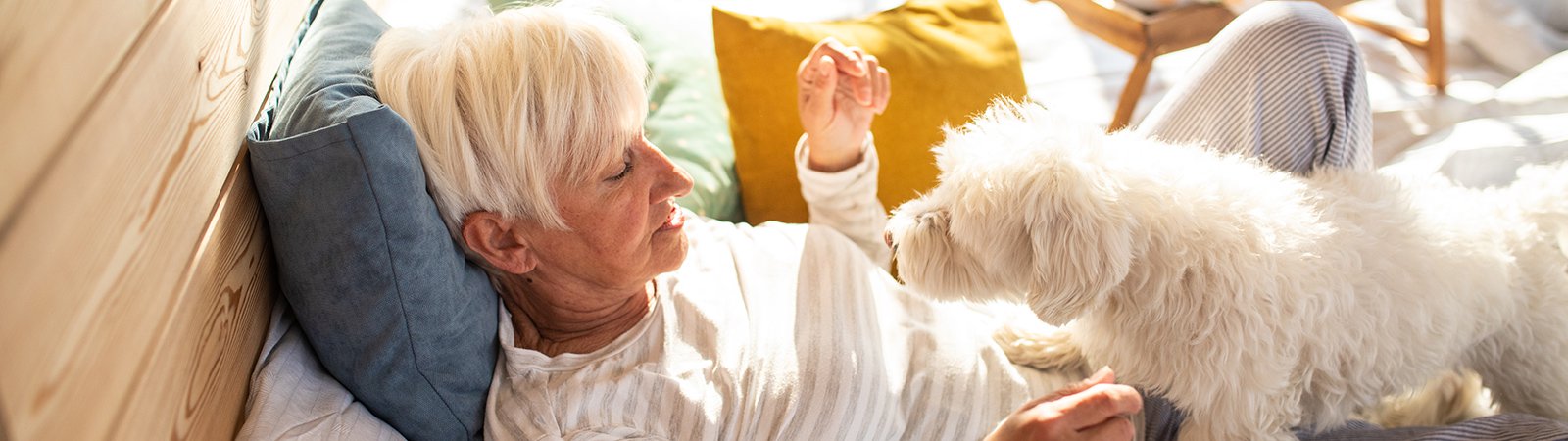 A woman  lying on bed with her white colour pet dog.