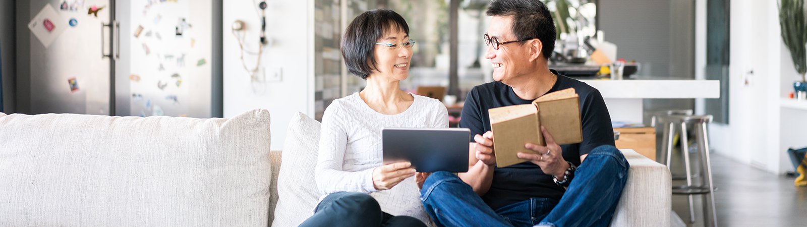 woman with tablet and man with book on couch