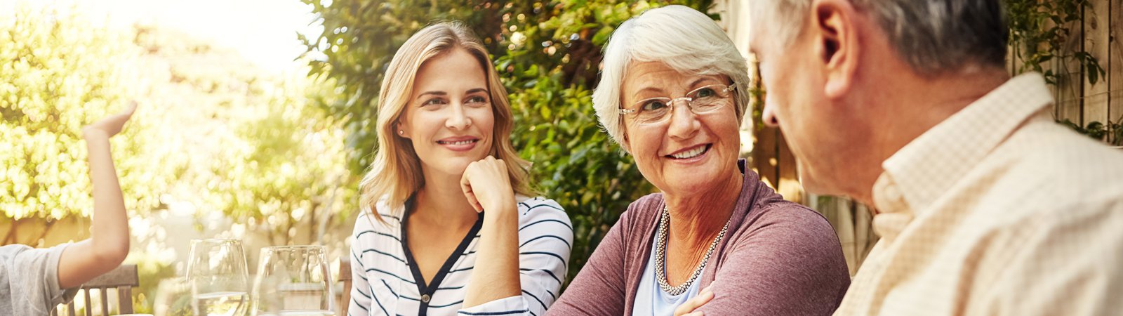 Young woman at outdoor table speaking with older parents